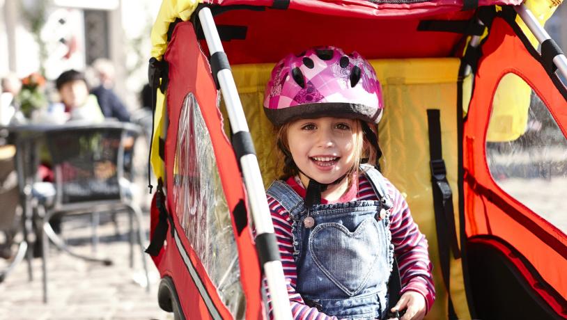 A young girl in a bike carriage with a pink helmet