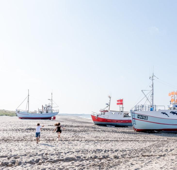 Barn som løper på stranden ved fiskebåter i Danmark